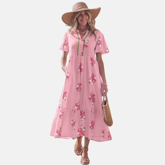 A woman wearing a light pink floral maxi dress with pink rose patterns, featuring flutter short sleeves and a notched neckline.