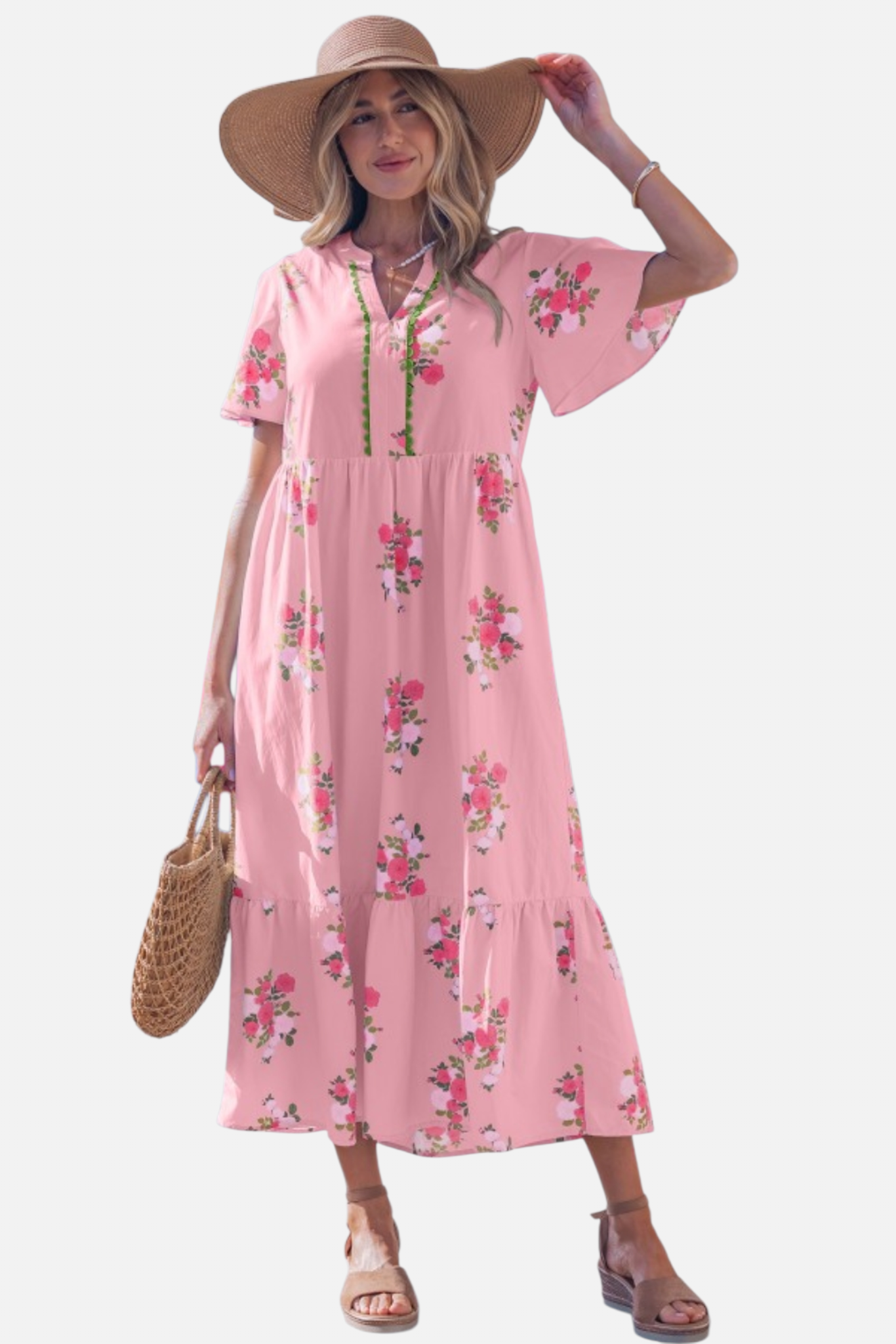 A woman wearing a light pink floral maxi dress with pink rose patterns, featuring flutter short sleeves and a notched neckline.