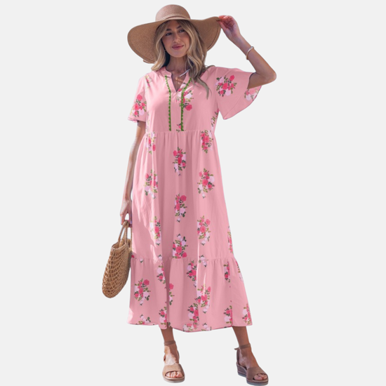 A woman wearing a light pink floral maxi dress with pink rose patterns, featuring flutter short sleeves and a notched neckline.