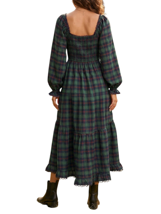 A woman shown from the back wearing a long-sleeve plaid midi dress in dark green, black, and red, paired with dark brown boots, against a plain white background.
