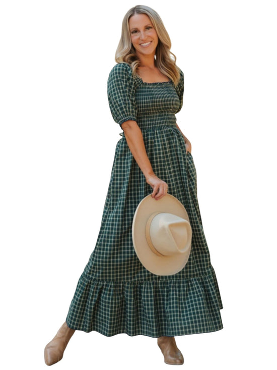 Woman wearing a green plaid dress holding a hat on a white background