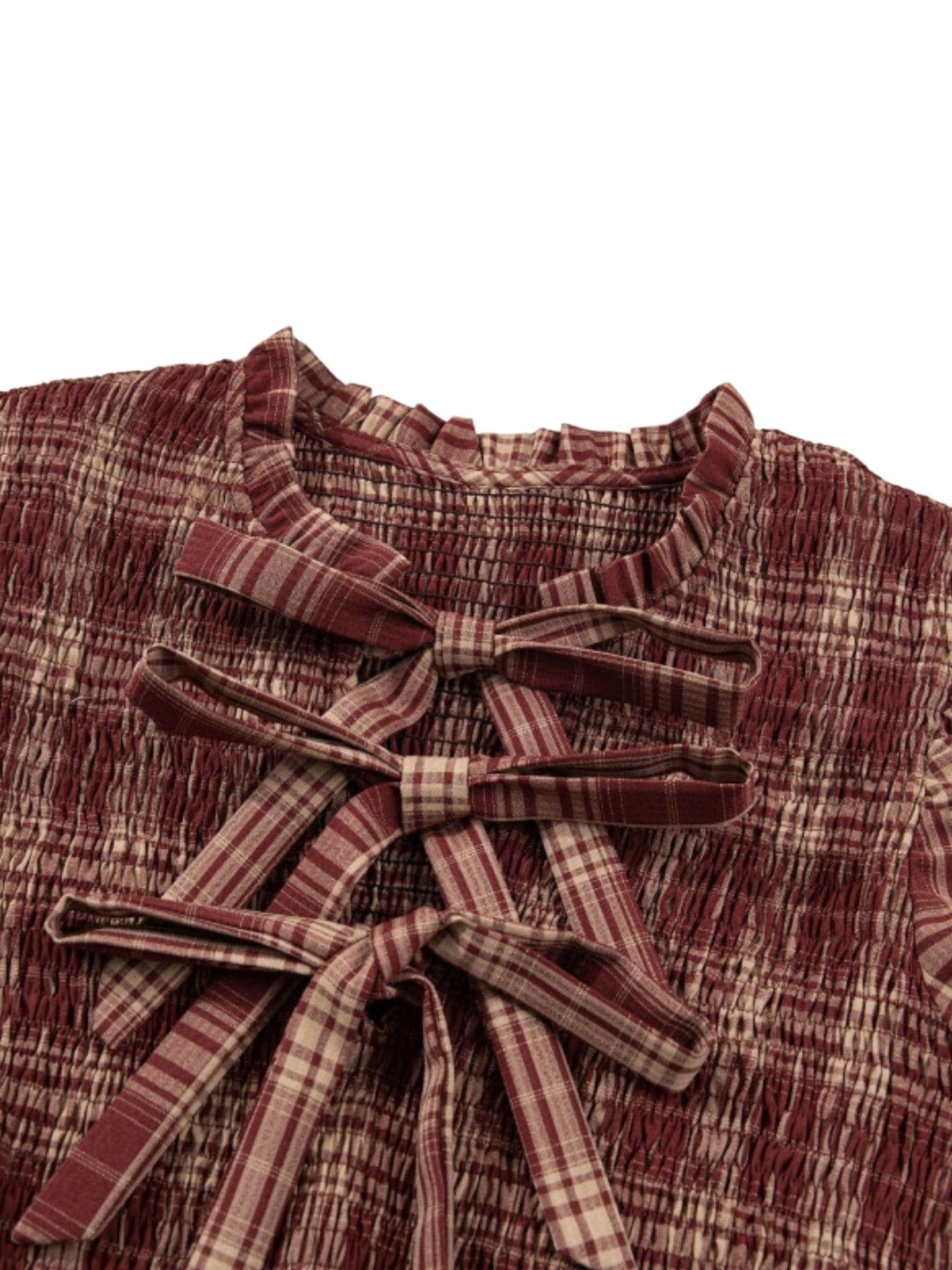 Close-up of a textured, smocked blouse in a rust red and beige plaid pattern, featuring a large matching plaid bow at the front neckline.
