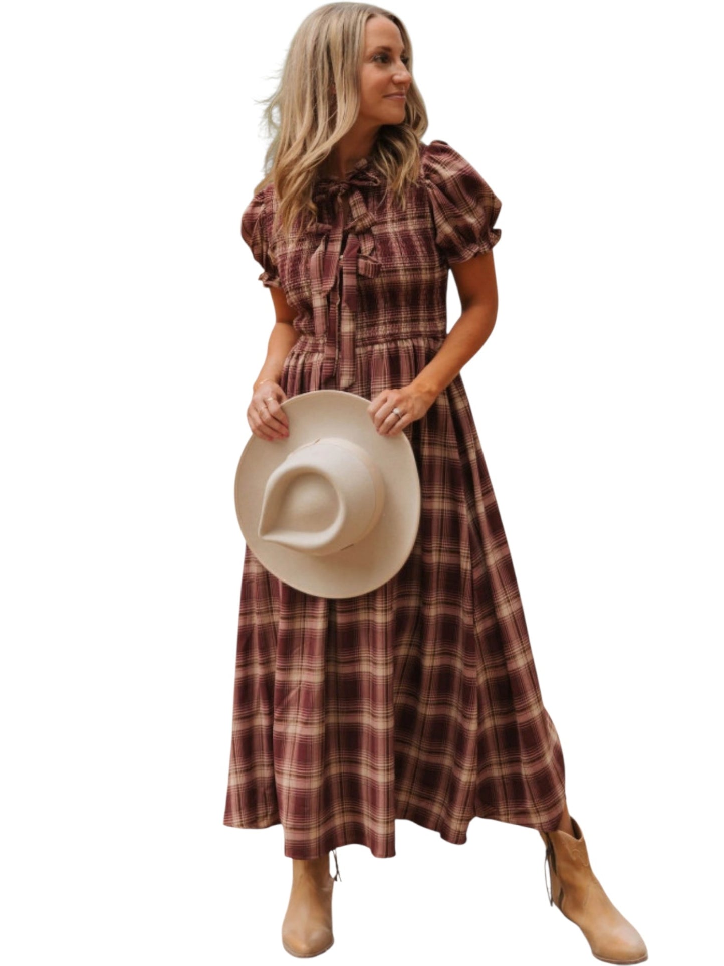A woman modeling a long-sleeve plaid midi dress in brown and burgundy tones, holding a beige cowboy hat, and wearing tan boots against a plain white background.