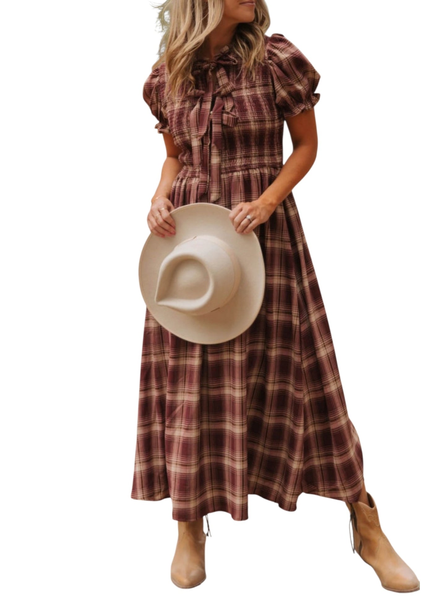 A woman wearing a long plaid midi dress in brown and burgundy tones, holding a beige wide-brim hat, against a plain white background.