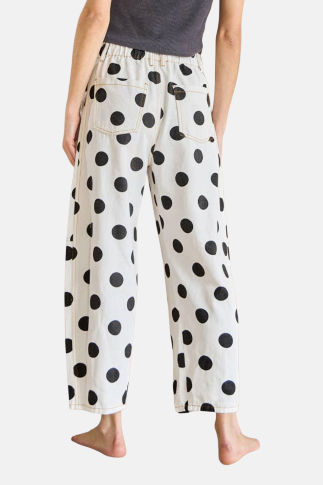 Back view of a model wearing white and black polka dot cropped jeans with visible contrast stitching.