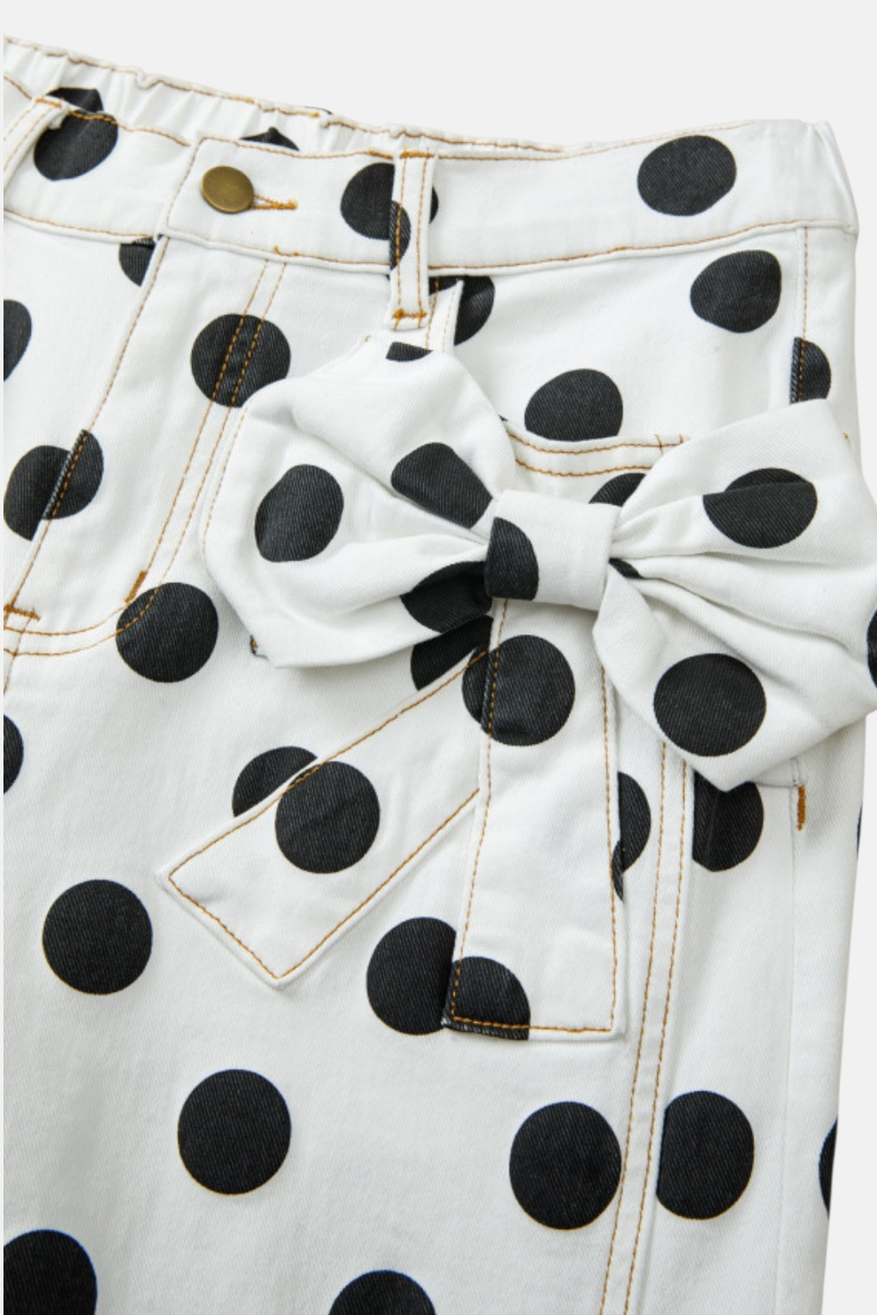 Close-up of the white denim fabric highlighting the intricate bow detail on the front pocket and bold black dots.