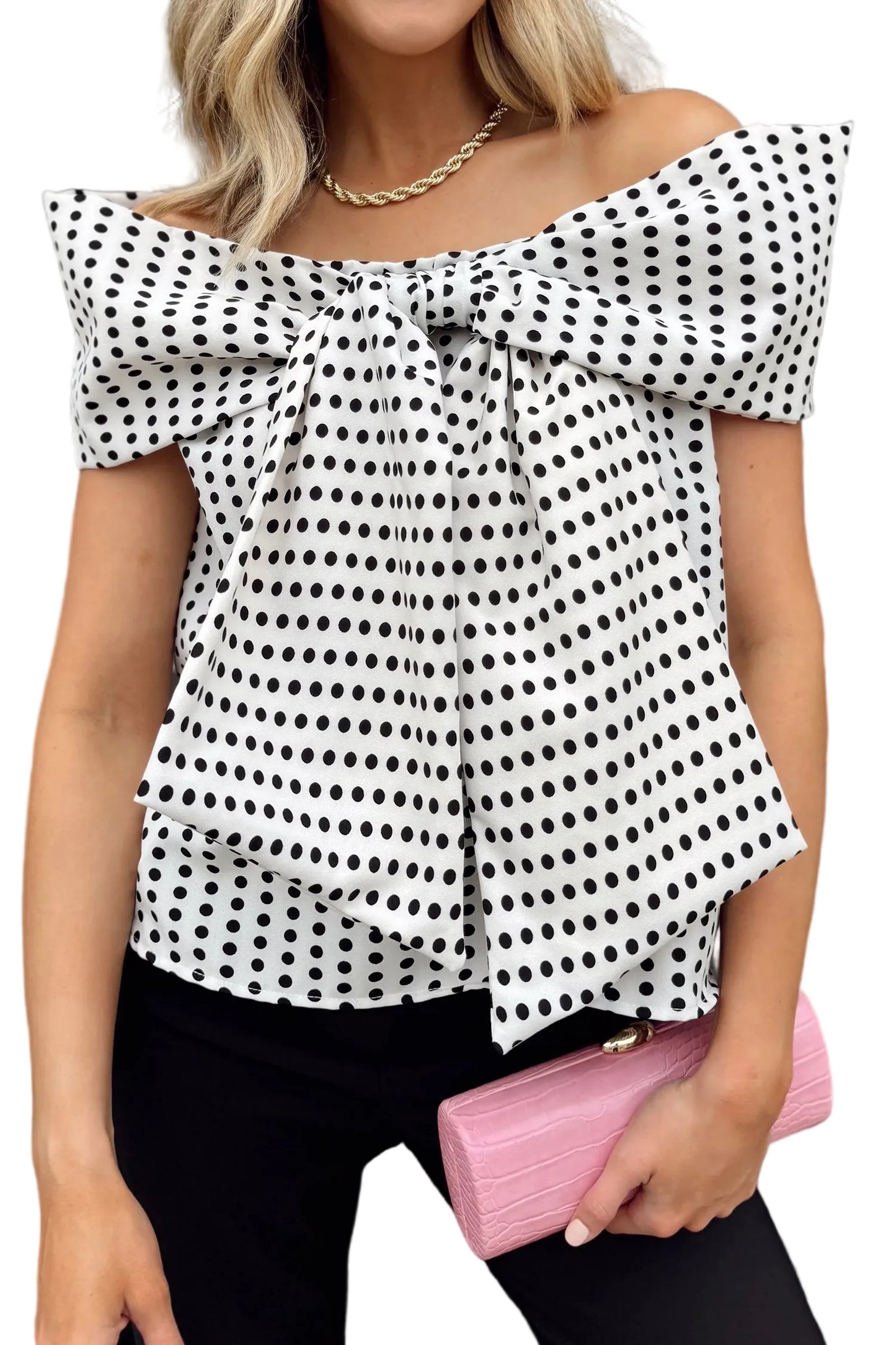 Woman wearing a black and white polka dot top with a pink clutch against a white background