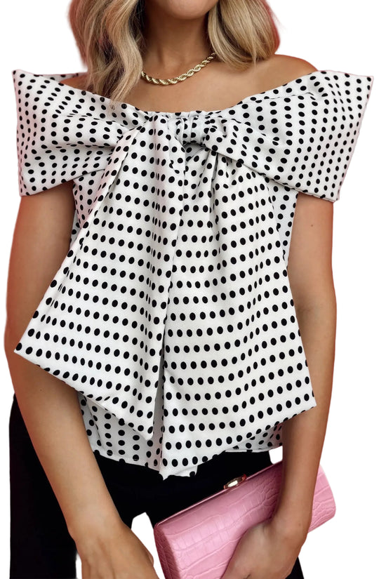 Woman wearing a polka dot blouse with a pink clutch against a white background
