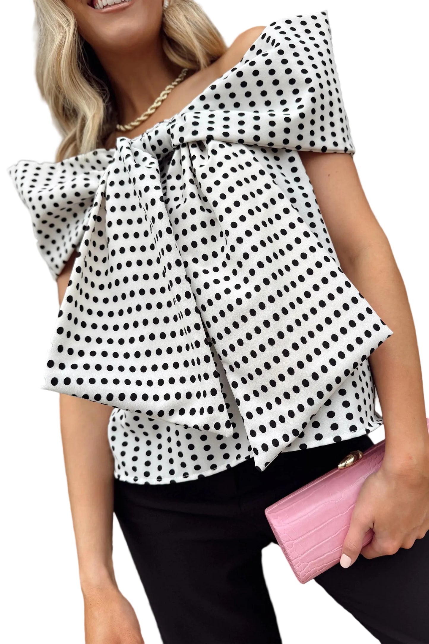 Woman wearing a polka dot blouse with a pink clutch against a white background