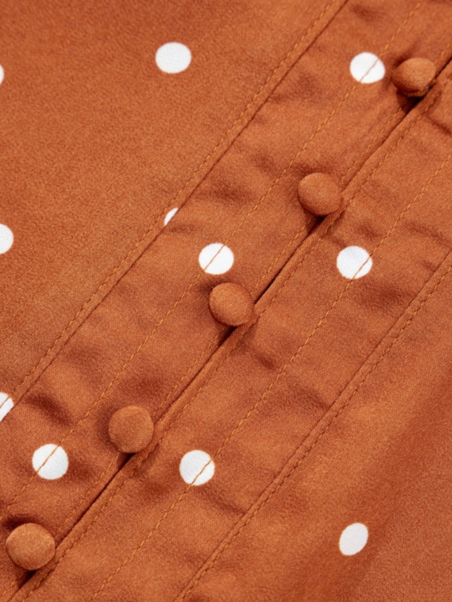 Close-up of a rust-brown fabric with white polka dots and matching fabric-covered decorative buttons along a front seam.