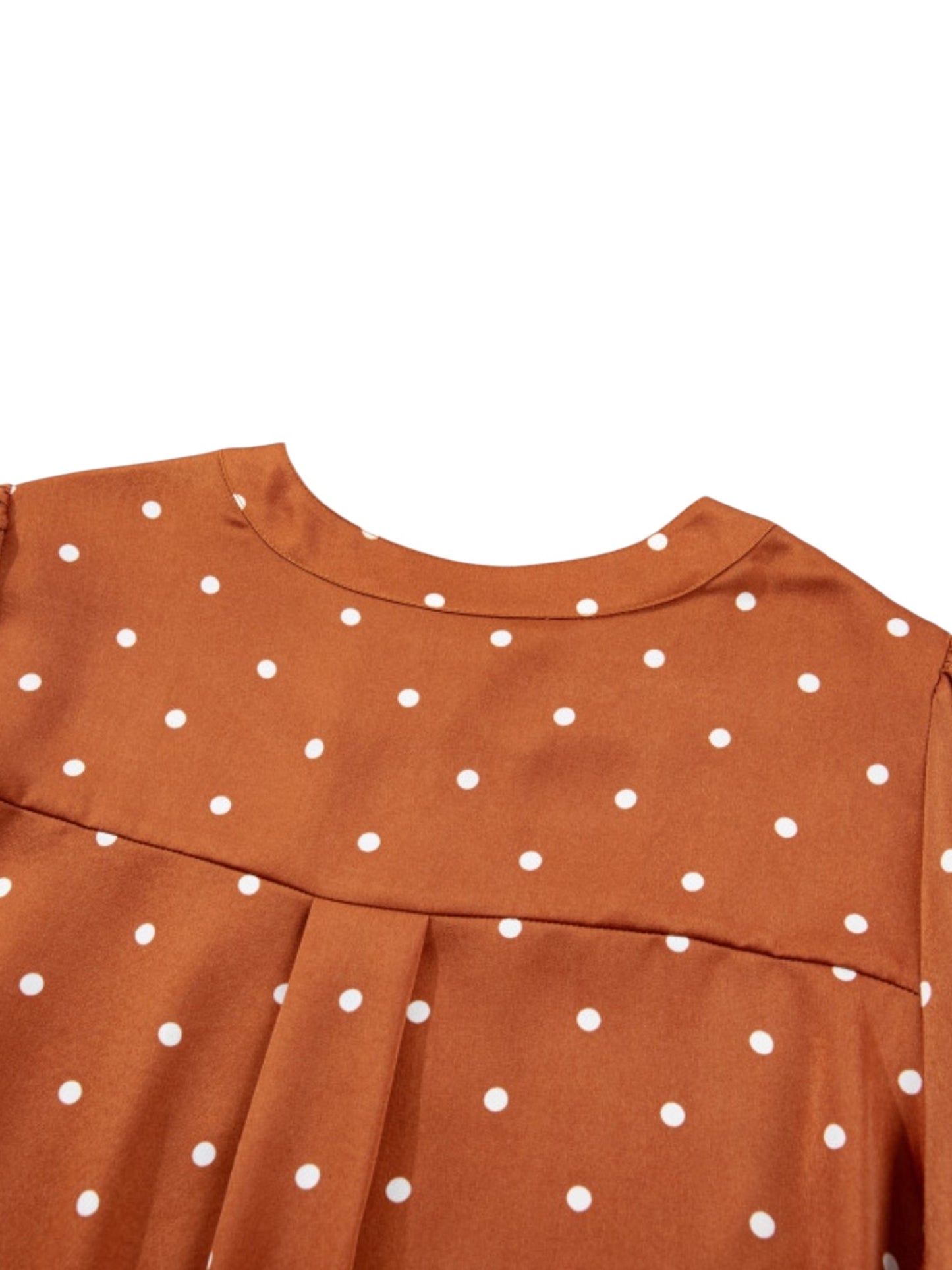 Close-up of a rust-orange dress with white polka dots, showing the back neckline and shoulder seam against a plain white background.