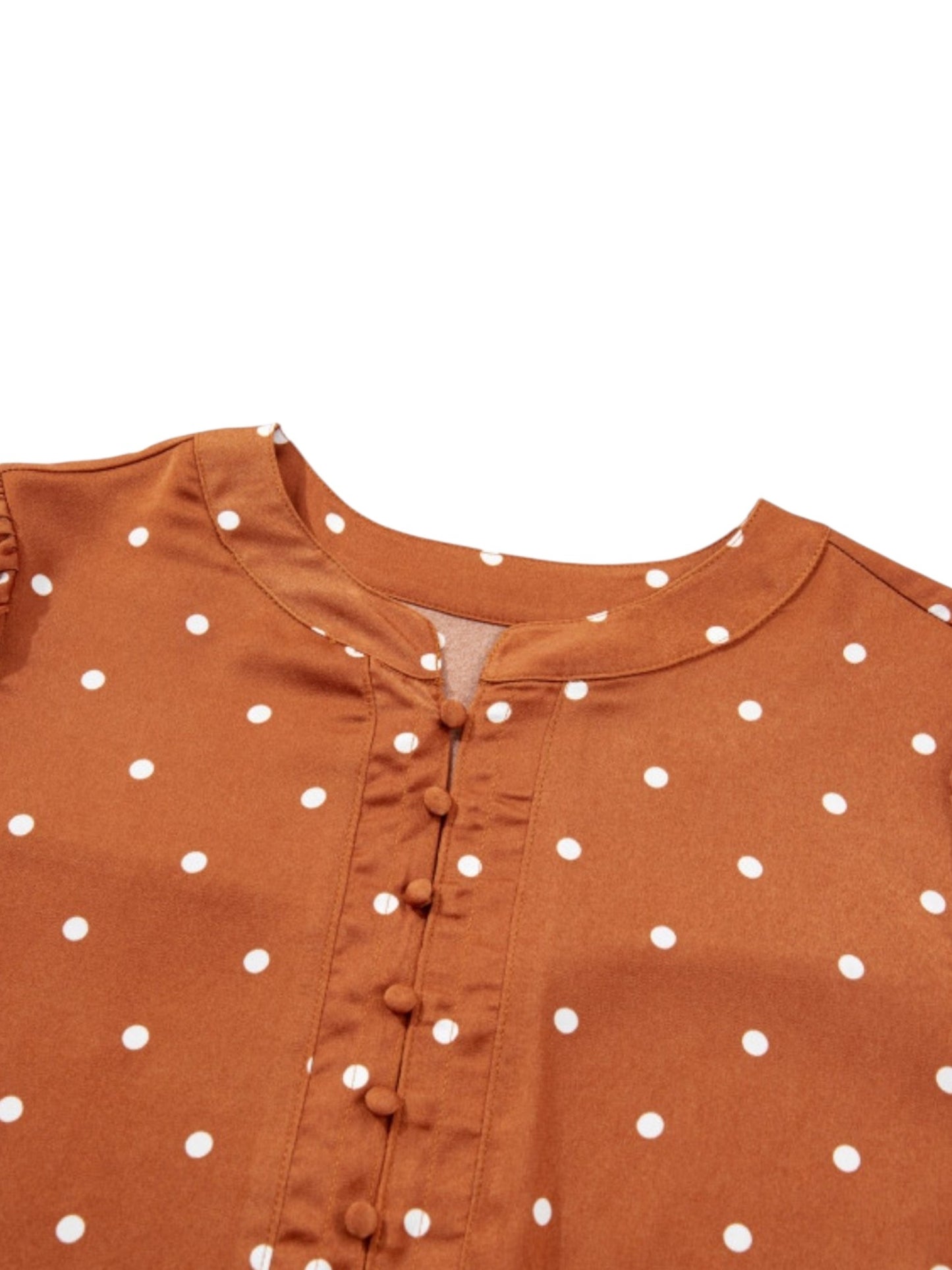 Close-up of a rust-orange garment with white polka dots and a button placket, shown against a plain white background.