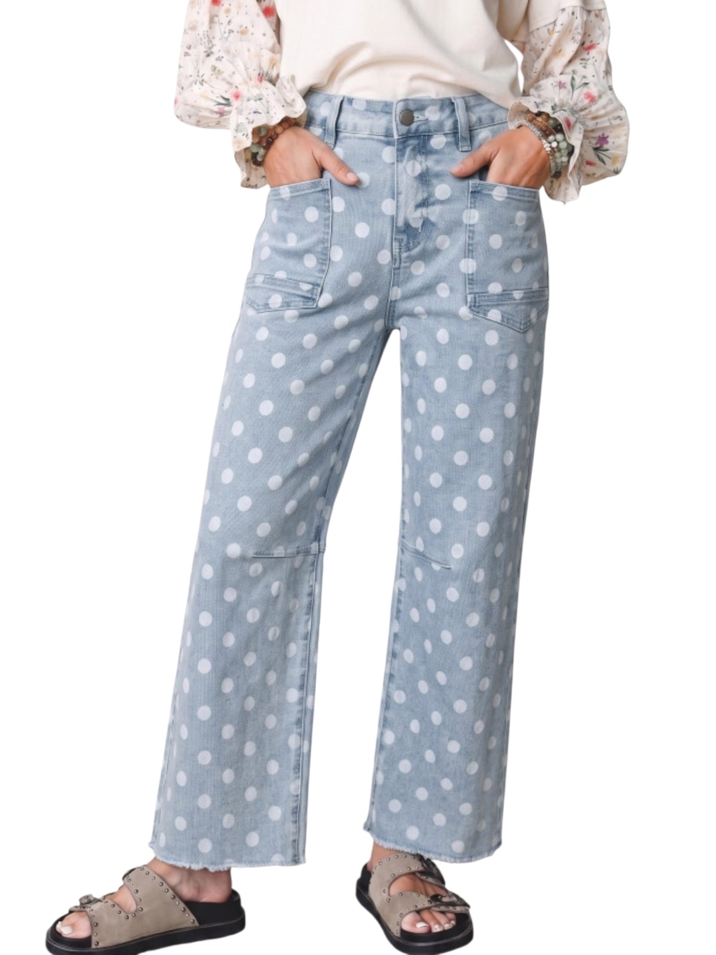 A person wearing light blue wide-leg denim jeans with a white polka dot pattern, styled with a cream blouse and brown slide sandals against a plain white background.