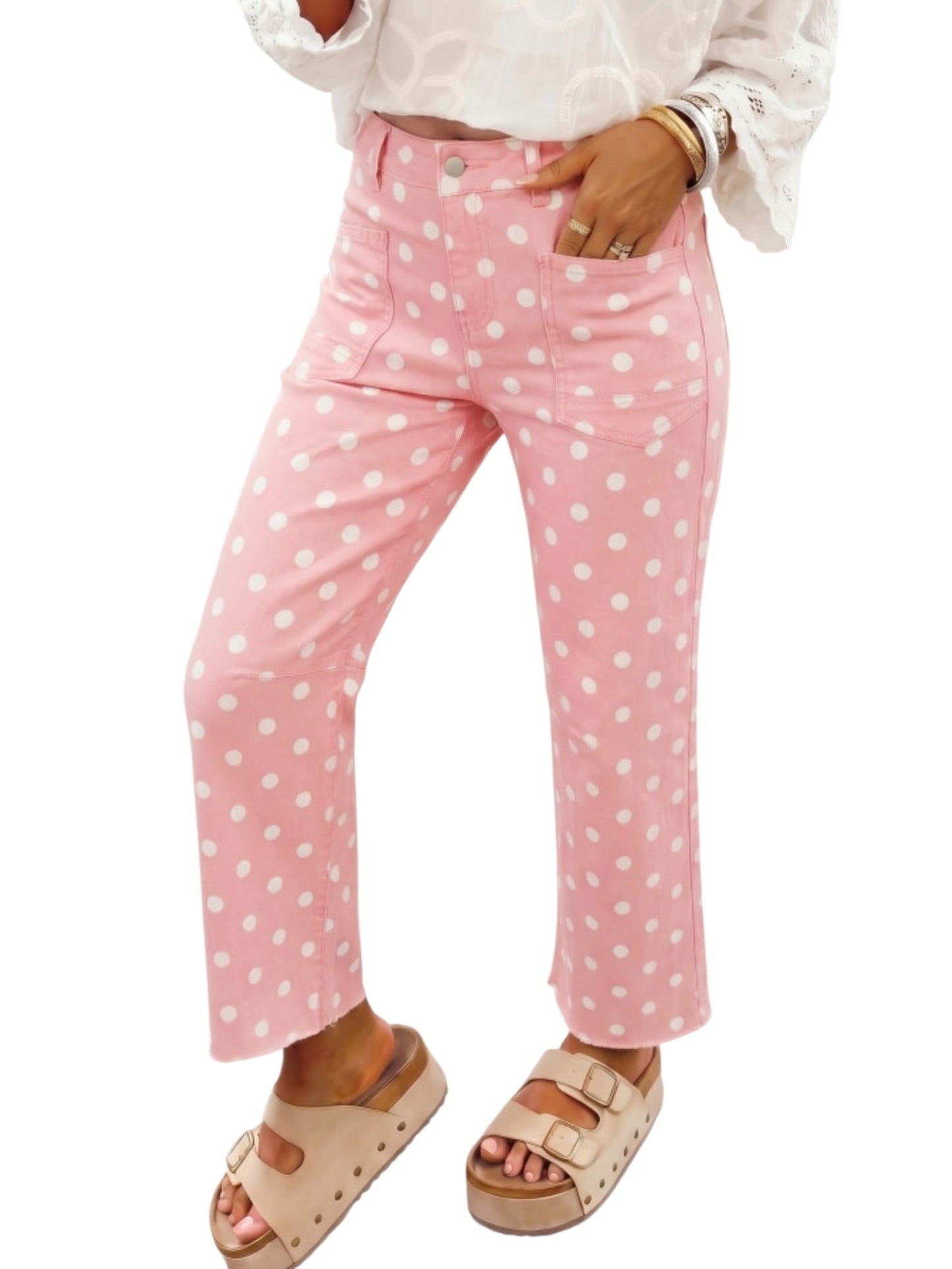 Pink cropped pants with a white polka dot pattern, modeled with a white blouse and beige platform sandals against a white background.