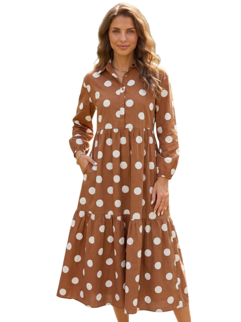 A woman modeling a brown long-sleeve midi dress with a white polka dot pattern, featuring a button-up front and tiered skirt, set against a plain white background.