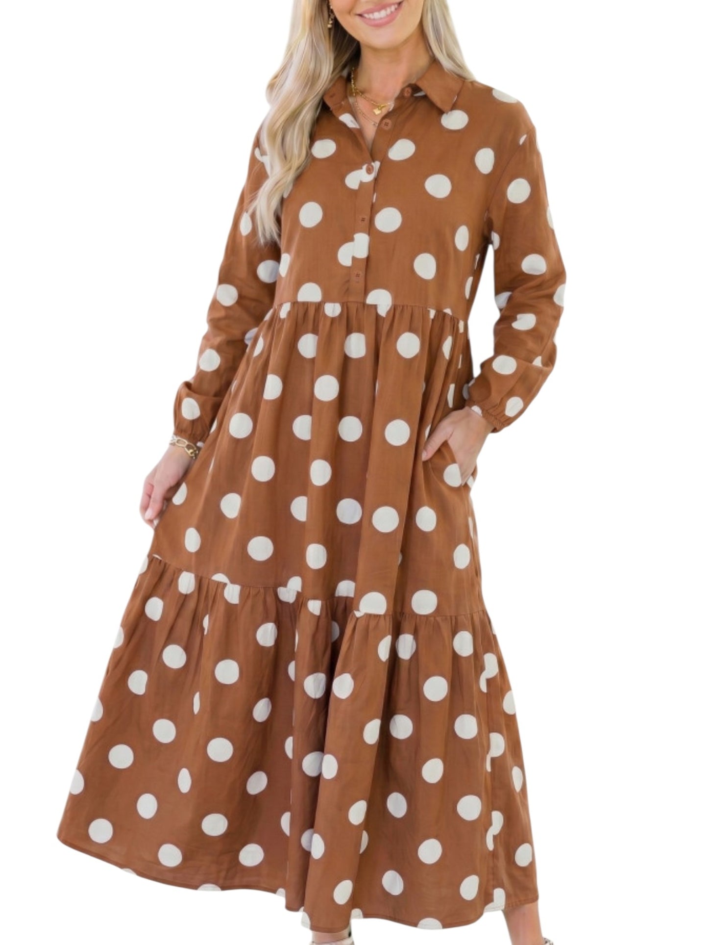 A woman wearing a long-sleeve brown tiered maxi dress with large white polka dots, shown against a plain white background.