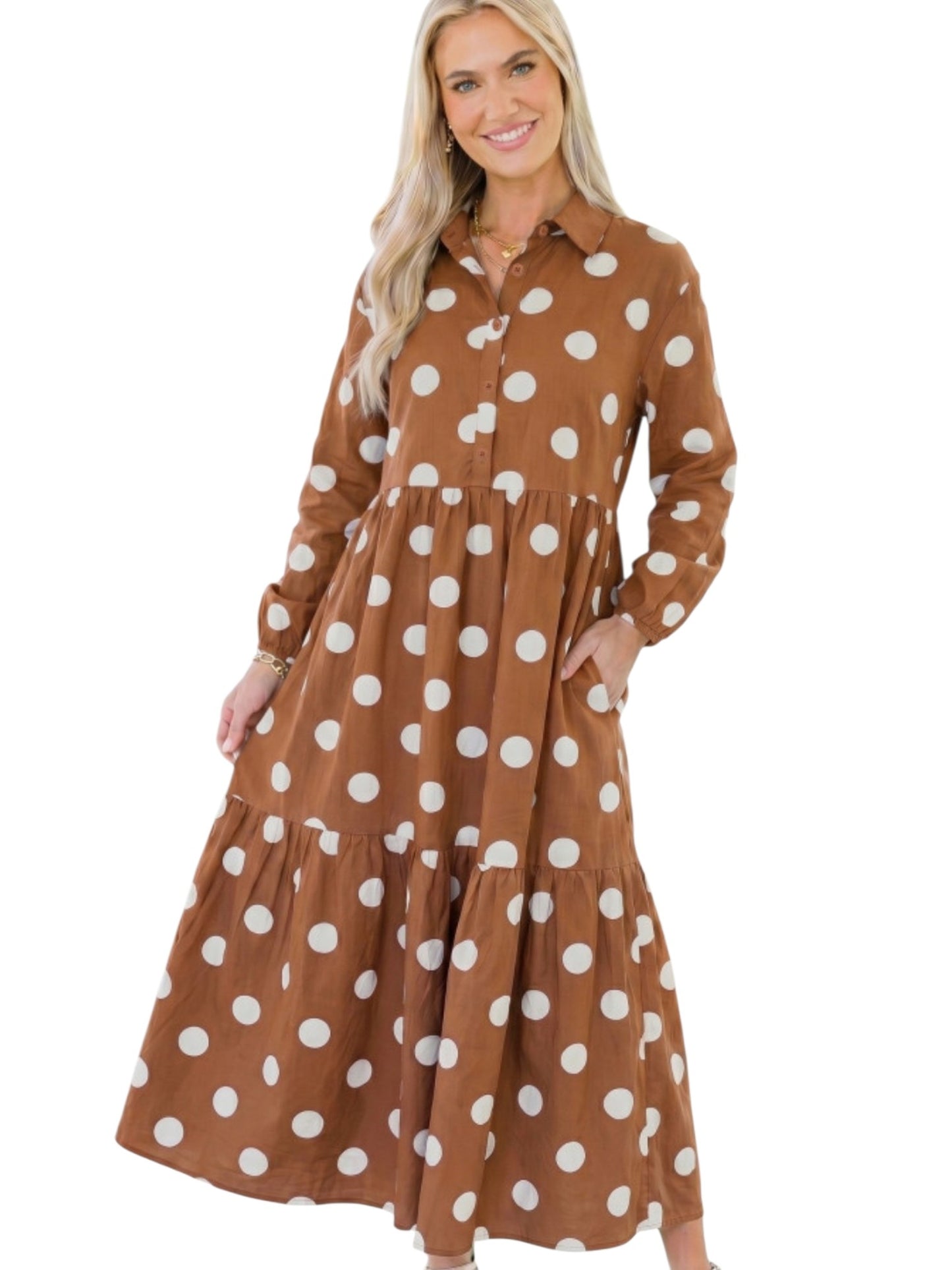A woman modeling a brown long-sleeve midi dress with a white polka dot pattern, featuring a button-down collar and tiered skirt, set against a plain white background.