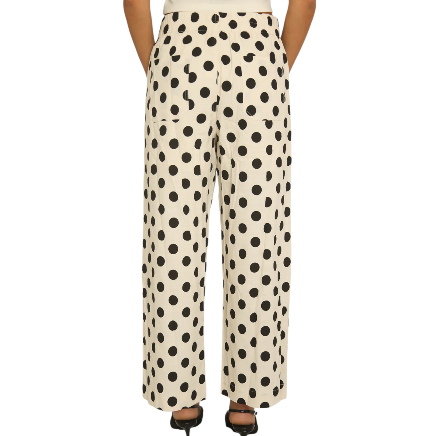 Back view of a woman wearing cream-coloured wide-leg trousers with a large black polka dot pattern, featuring a button closure and front patch pockets.