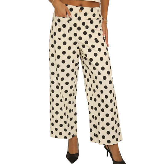 Front view of a woman wearing cream-coloured wide-leg trousers with a large black polka dot pattern, featuring a button closure and front patch pockets.