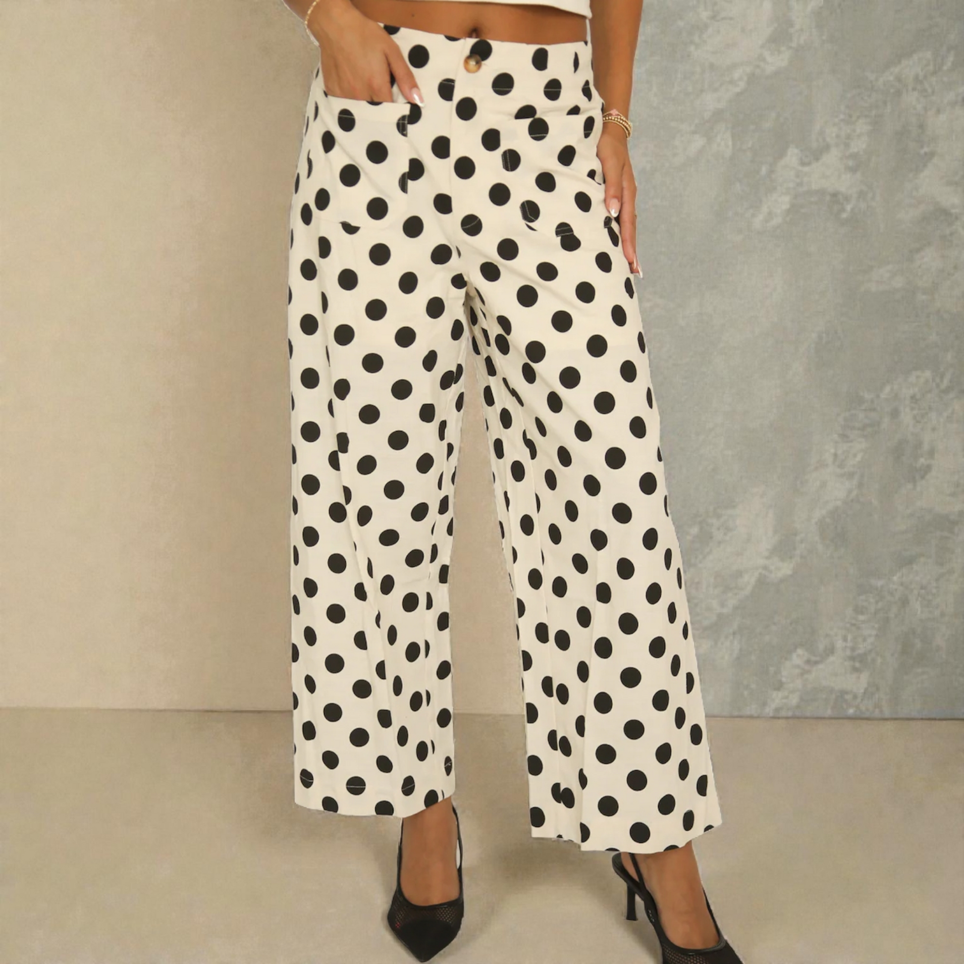 Front view of a woman wearing cream-coloured wide-leg trousers with a large black polka dot pattern, featuring a button closure and front patch pockets.