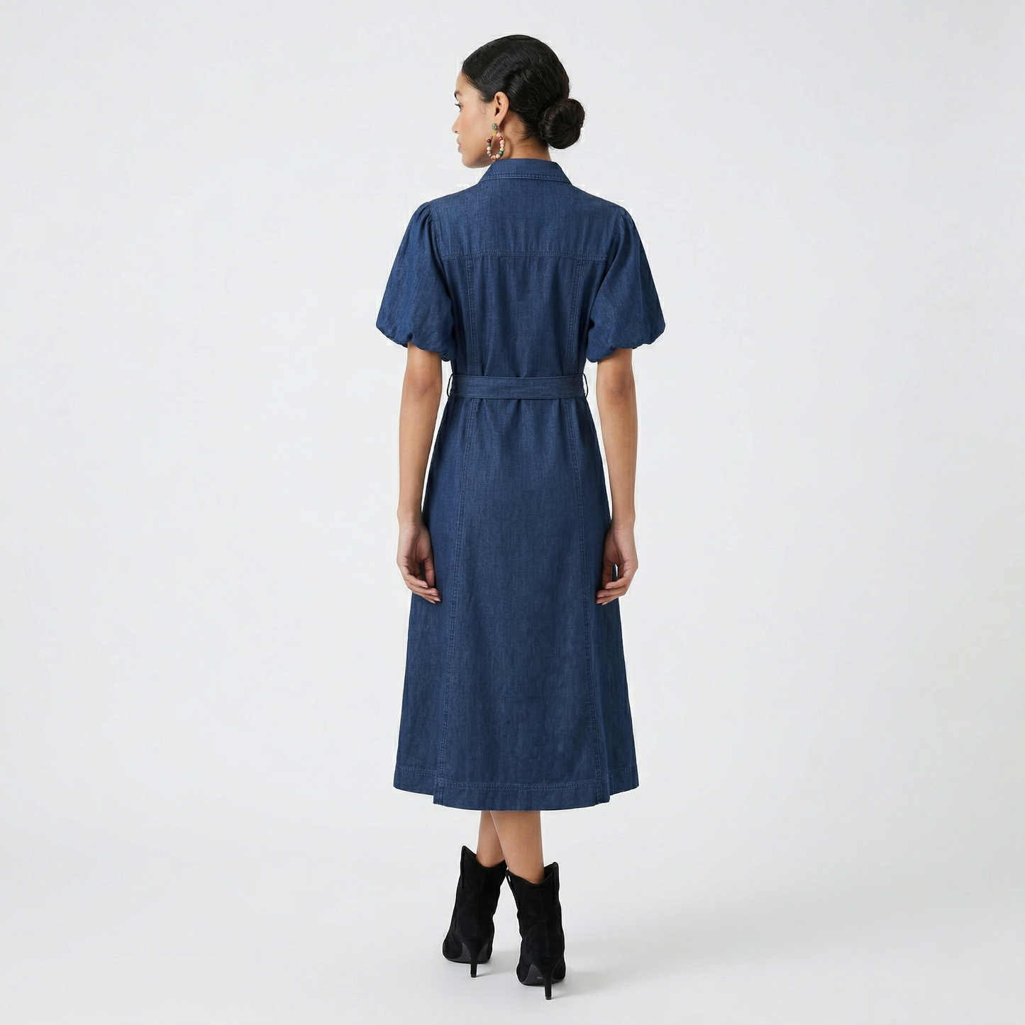 Rear view of a model wearing a deep indigo denim midi dress, showing the structured back yoke and the flowy A-line skirt.
