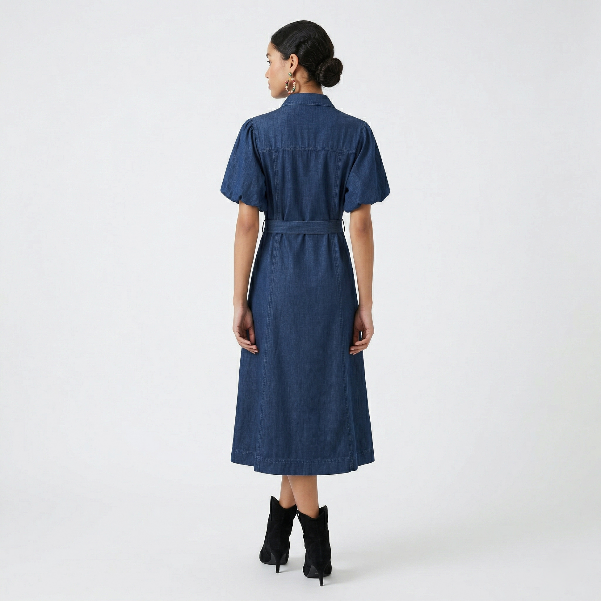 Rear view of a model wearing a deep indigo denim midi dress, showing the structured back yoke and the flowy A-line skirt.