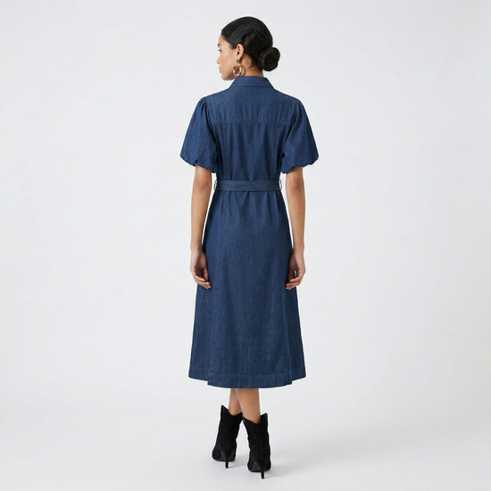 Rear view of a model wearing a deep indigo denim midi dress, showing the structured back yoke and the flowy A-line skirt.