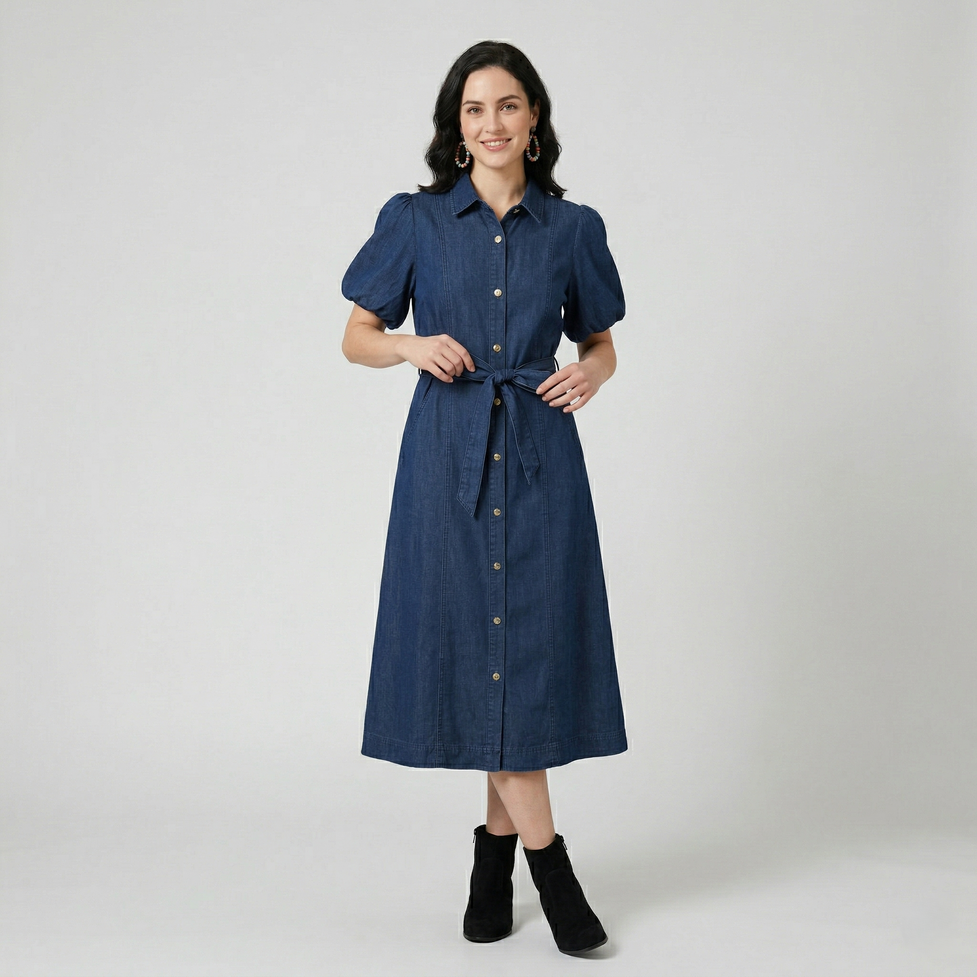 Front view of a model in a dark wash denim shirt dress featuring voluminous puff sleeves and a self-tie bow at the waist.