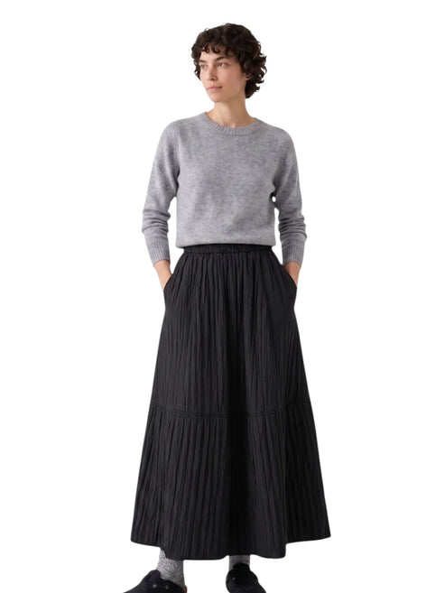 Full-length shot of the model wearing the black textured A-line maxi skirt with grey socks and clogs for a casual winter look.