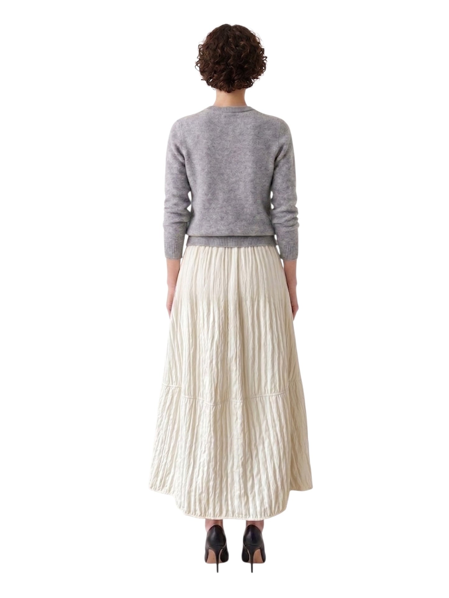 Person wearing a gray sweater and ivory pleated skirt on a white background