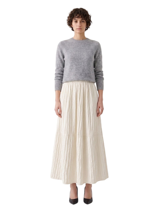 Front full-length view of a model styling an ivory textured quilted A-line maxi skirt with a grey knit jumper and heels.