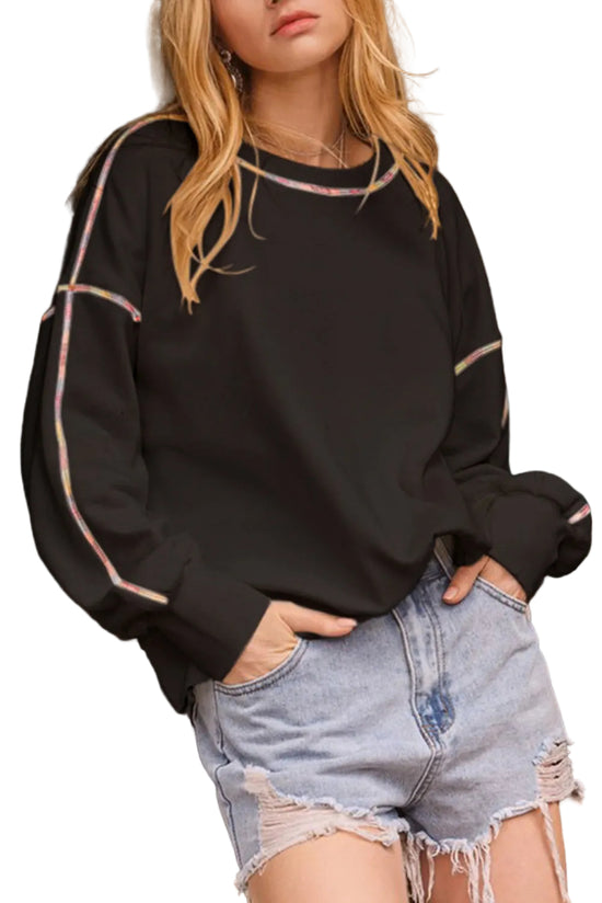 Person wearing a black sweater with pink accents and denim shorts standing in front of a white background.