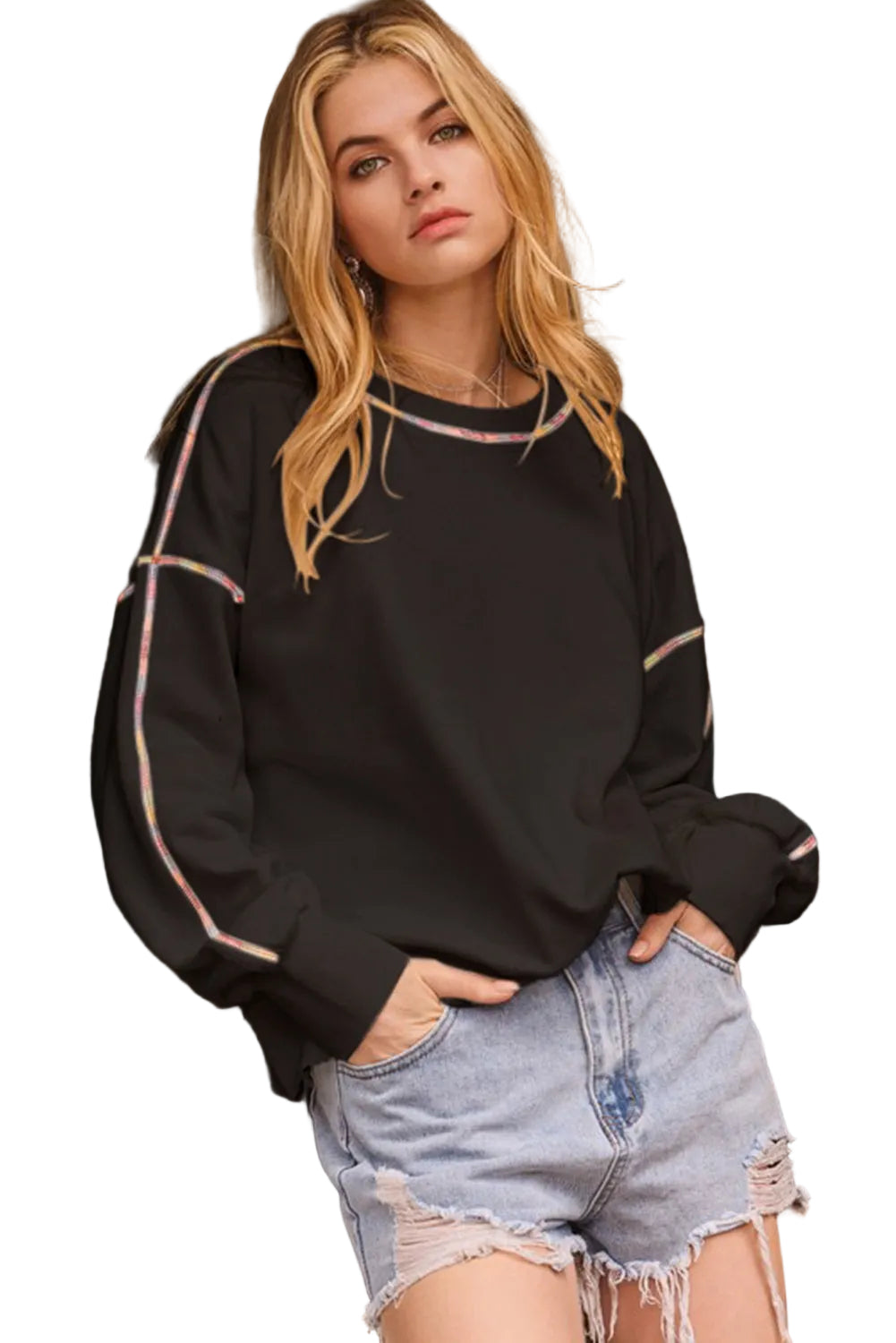 Woman wearing a black sweatshirt with white trim and denim shorts standing in in front of a white background.
