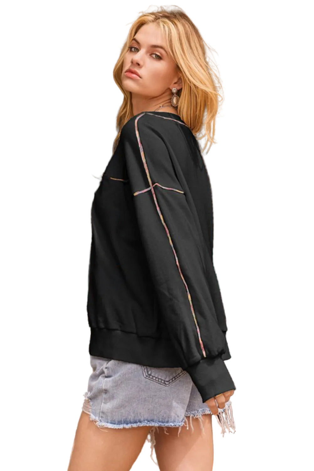 Woman wearing a black sweatshirt and denim shorts standing in front of a white background.