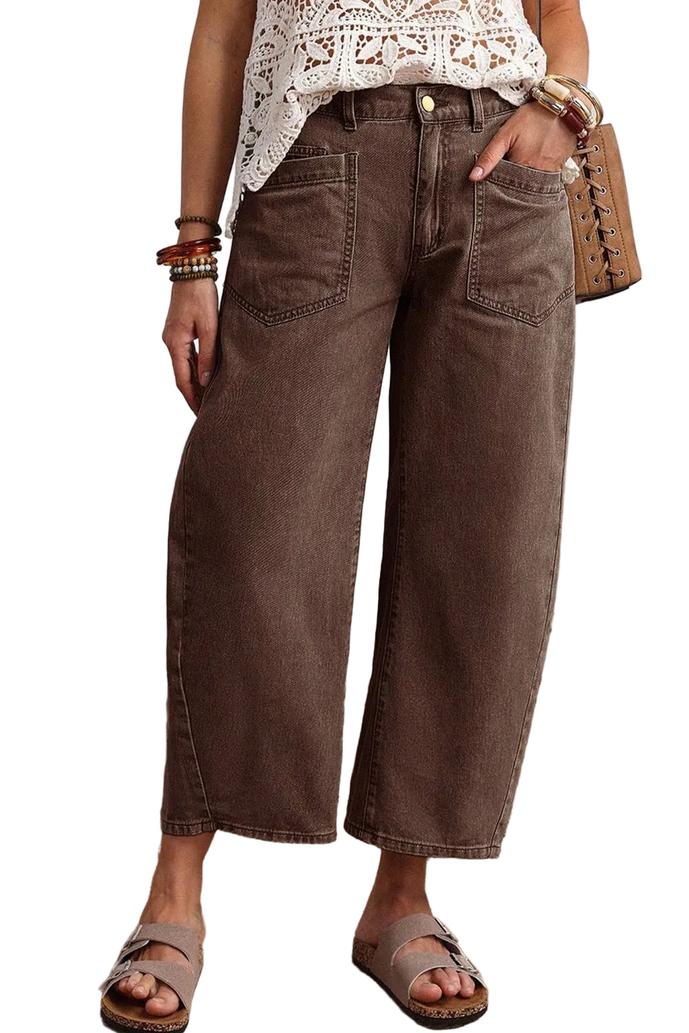 Person wearing brown wide-leg jeans with a white lace top and sandals on a neutral background