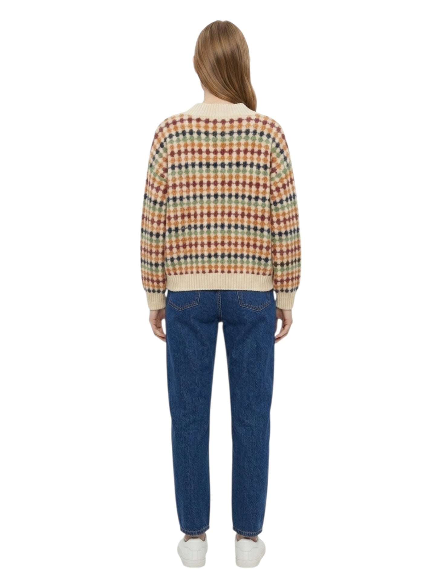 A woman viewed from the back wearing a cream knit cardigan with a multicolor plaid pattern, blue jeans, and white sneakers, set against a plain white background.