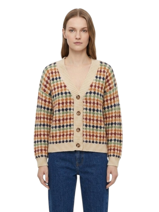 A woman modeling a cream-colored knit cardigan with a multicolor geometric pattern in red, orange, yellow, and green, paired with blue jeans against a plain white background.