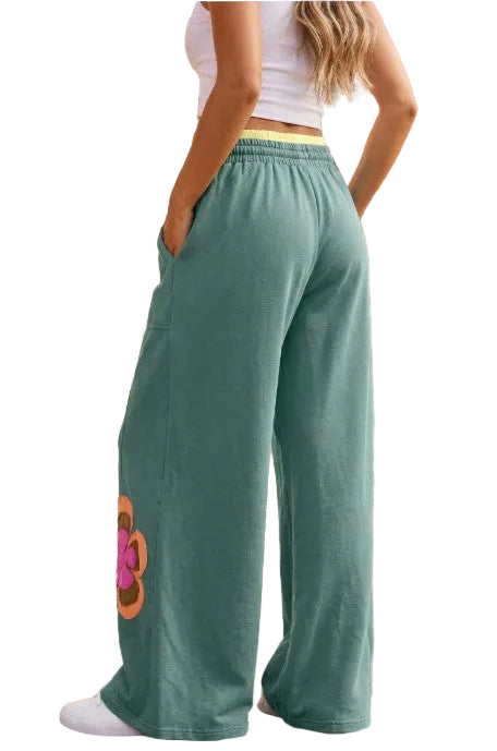 The rear view of the green patchwork pants, showing the clean, flowing wide-leg silhouette and the contrast yellow elastic waistband.