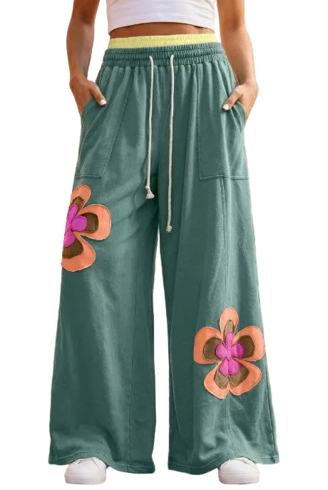 A front-facing product shot of the forest green wide-leg lounge pants, featuring the large peach and brown flower patches and the yellow drawstring waist.