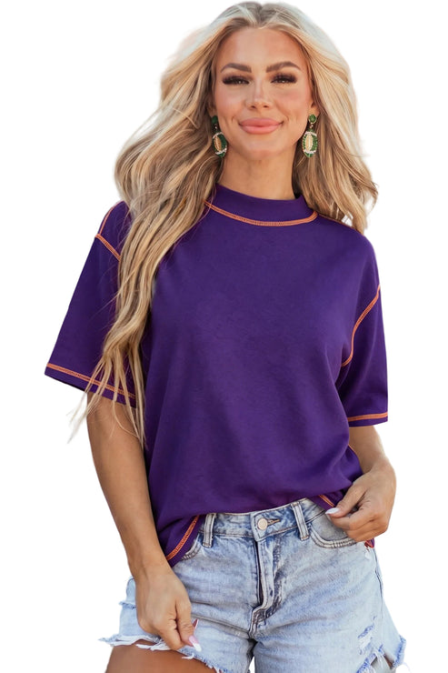 Model wearing a purple mock neck oversized t-shirt featuring bright orange contrast stitching along the seams and dropped shoulders.