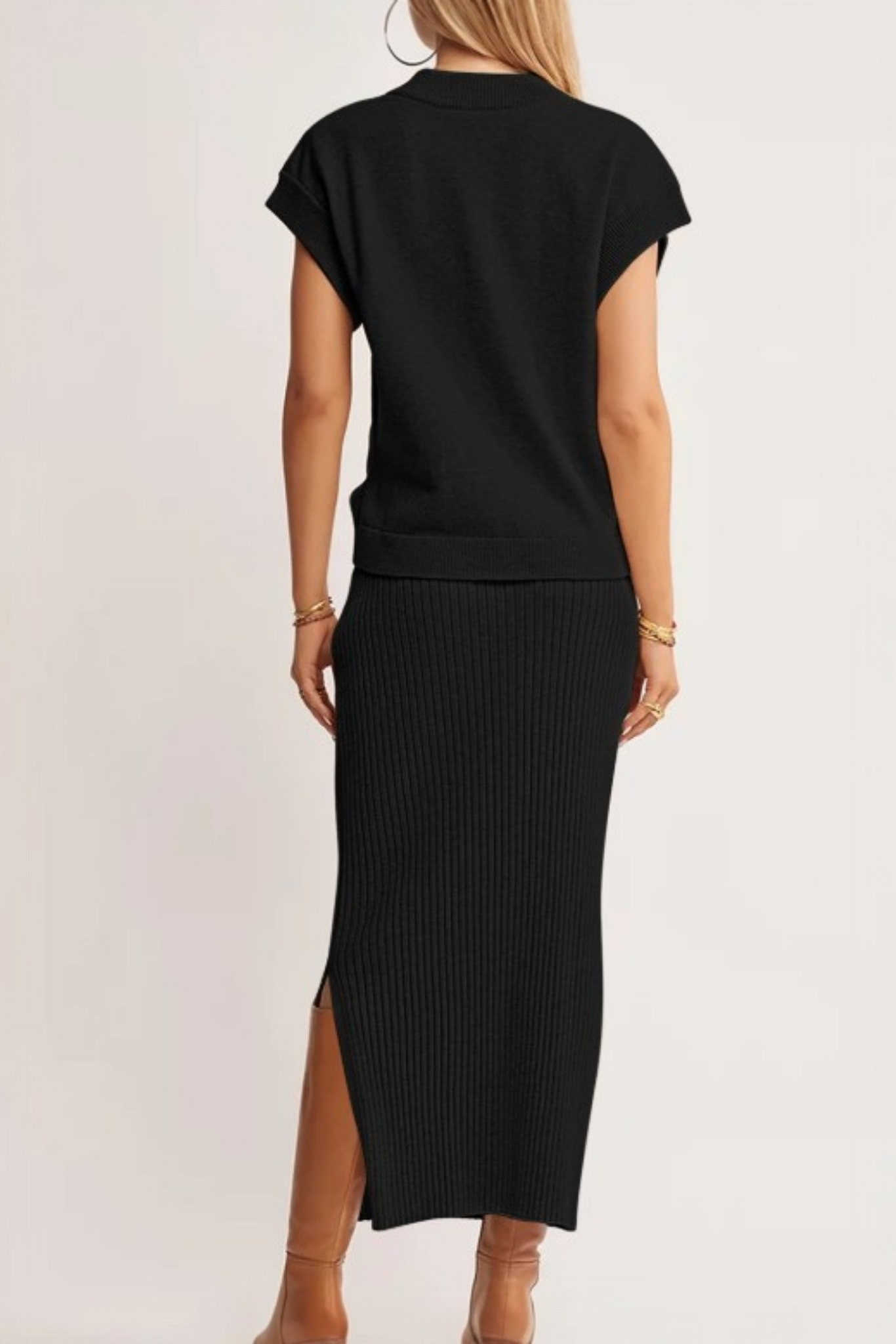 A rear view of a model in a black ribbed knit two-piece set, highlighting the midi-length skirt's side slit and the relaxed drape of the dolman tee.