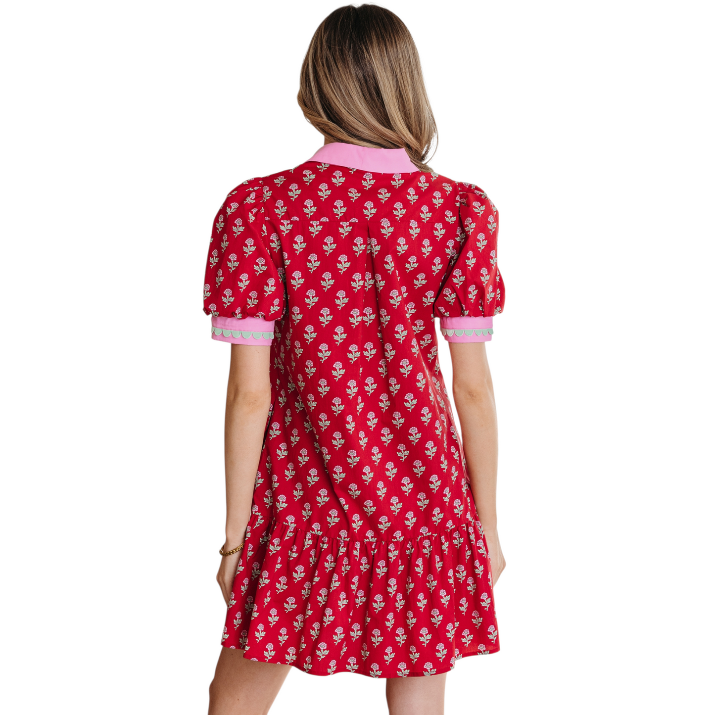 Woman wearing a red floral cotton mini dress with pink ricrac trim, V-neckline, and puff sleeves. Back view.