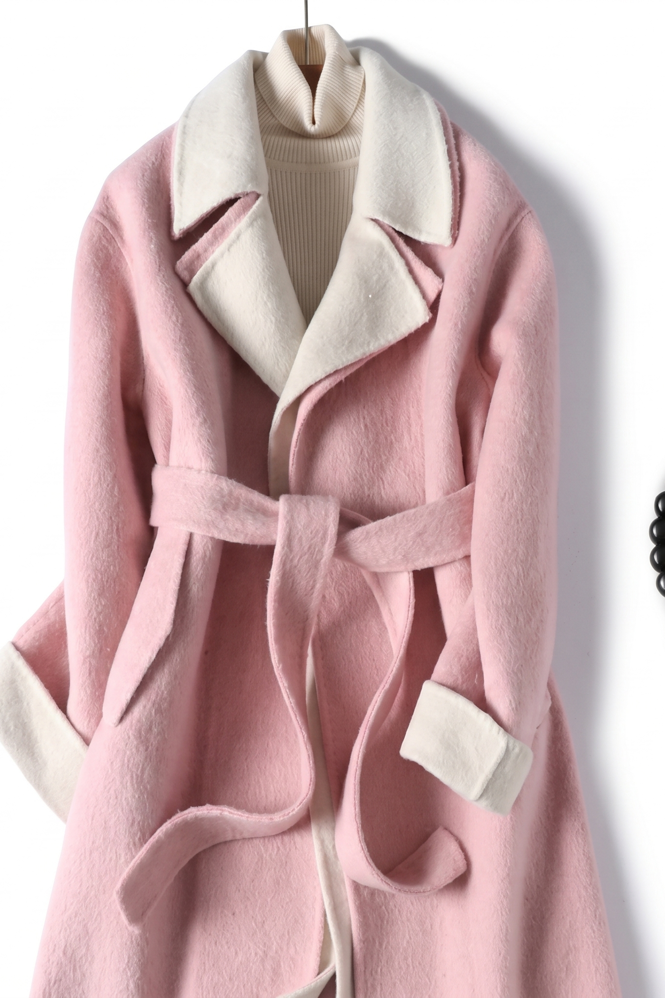 Front view of a dusty rose pink wool wrap coat featuring a cream-colored notched lapel and matching self-tie waist belt styling with a woven handle bag.