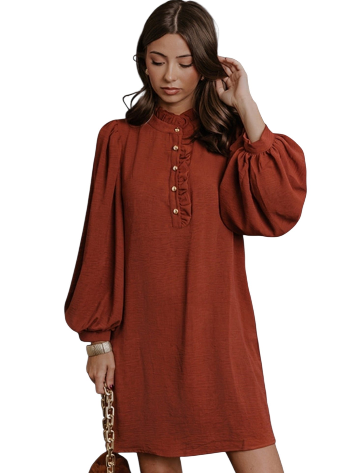 A woman wearing a rust-orange long-sleeve dress with a high ruffled collar and gold buttons down the front, holding a small brown handbag with a gold chain strap against a plain white background.
