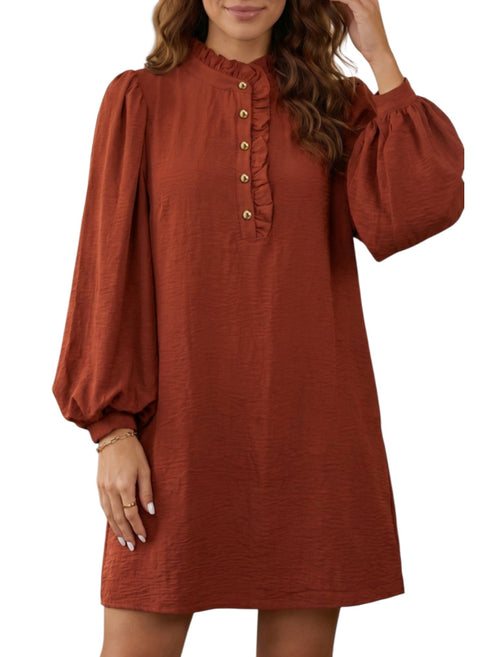 A woman wearing a rust-colored long-sleeve dress with a ruffled mock neck and decorative gold buttons down the front, shown against a plain white background.