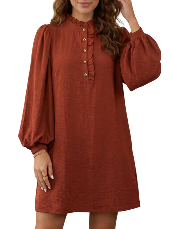 A woman wearing a rust-colored long-sleeve dress with a ruffled mock neck and decorative gold buttons down the front, shown against a plain white background.