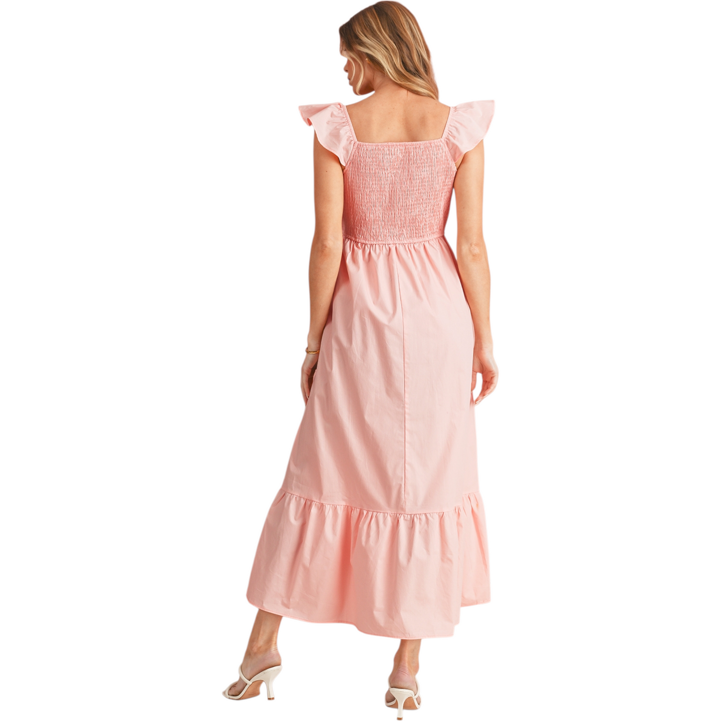 Back view of a woman wearing a peach-pink cotton maxi dress featuring a shirred elastic bodice, ruffle cap sleeves, and a tiered A-line skirt. 