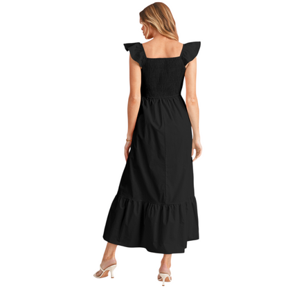 Back view of a woman wearing a black 100% cotton maxi dress with a smocked elastic bodice, feminine ruffle shoulder straps, and a tiered flowy skirt.