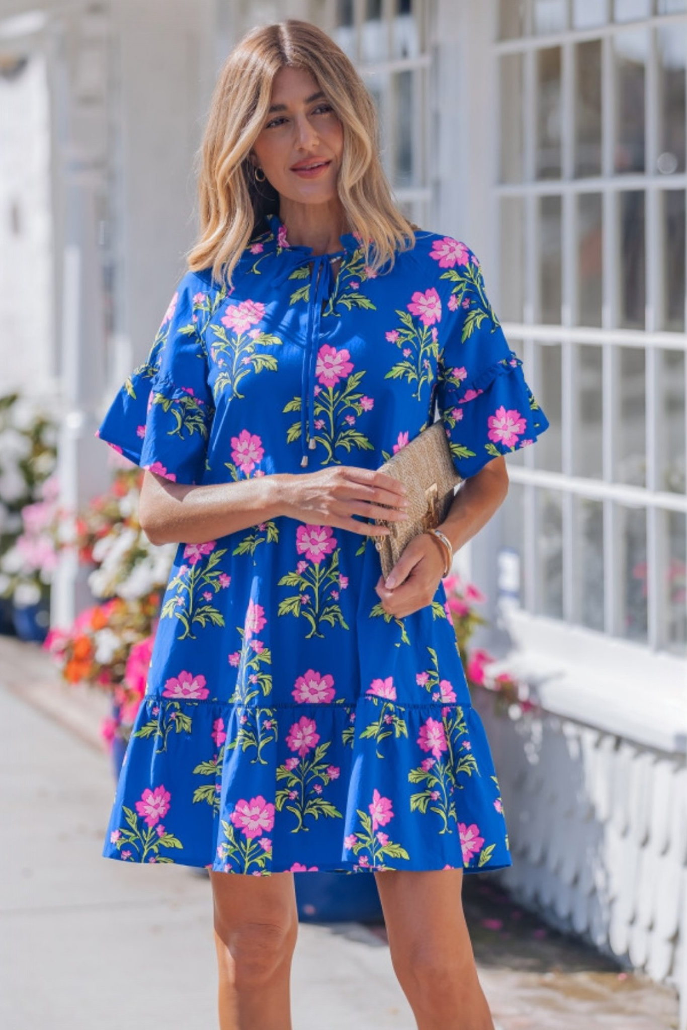 Lifestyle shot of the vibrant floral mini dress in an outdoor setting, styled with a straw clutch for a perfect casual outing or garden party look.