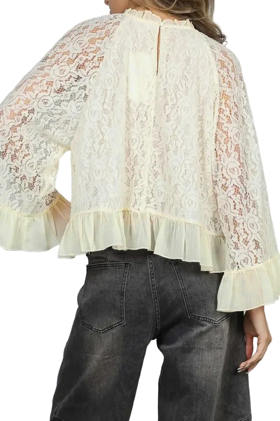 White lace blouse with ruffled sleeves and hem worn by a person against a plain background